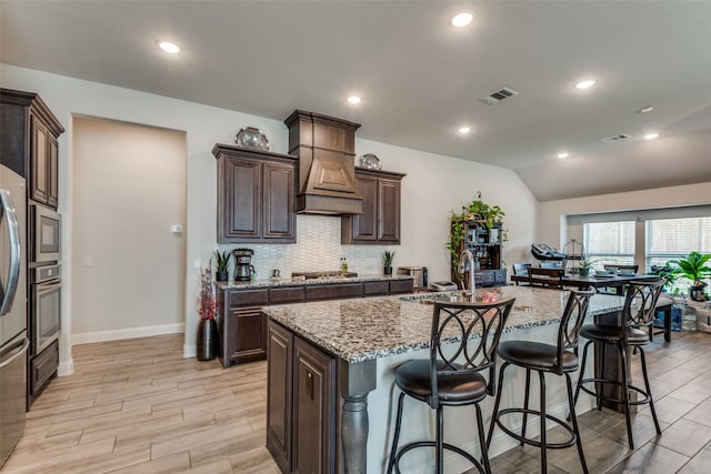 kitchen featuring light stone countertops, vaulted ceiling, appliances with stainless steel finishes, and a kitchen island with sink