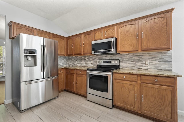 kitchen with a textured ceiling, backsplash, appliances with stainless steel finishes, light stone countertops, and vaulted ceiling