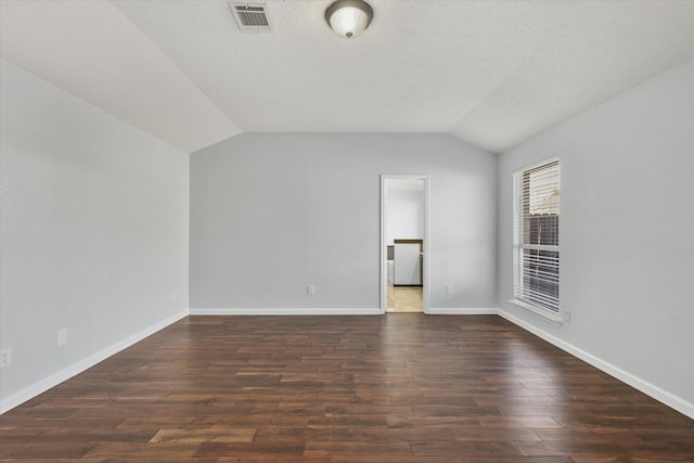 unfurnished room with vaulted ceiling, a textured ceiling, and dark hardwood / wood-style floors