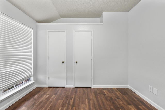 unfurnished bedroom with vaulted ceiling, a textured ceiling, dark hardwood / wood-style flooring, and multiple windows