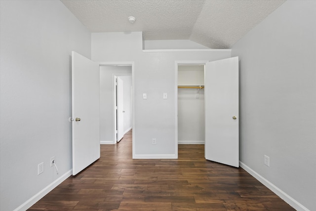 unfurnished bedroom with a spacious closet, lofted ceiling, a textured ceiling, and dark wood-type flooring