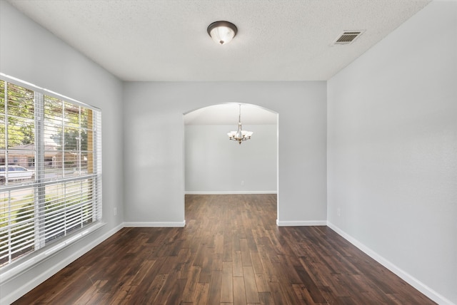 empty room with a notable chandelier, dark hardwood / wood-style floors, and a textured ceiling