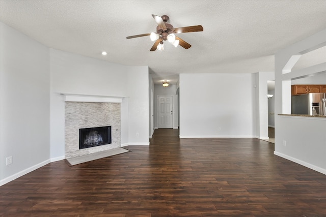 unfurnished living room featuring a textured ceiling, a fireplace, dark hardwood / wood-style flooring, and ceiling fan