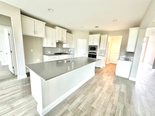 kitchen featuring white cabinetry, stainless steel appliances, light wood-type flooring, a center island with sink, and sink