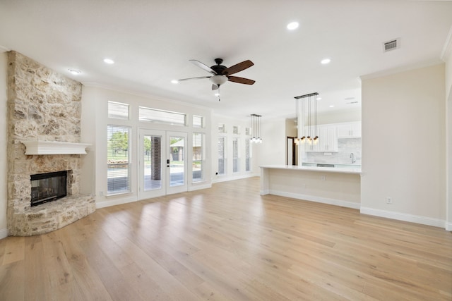 unfurnished living room with french doors, light hardwood / wood-style flooring, a fireplace, ceiling fan with notable chandelier, and crown molding