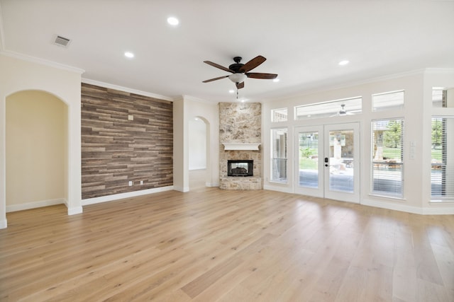 unfurnished living room featuring ceiling fan, french doors, a stone fireplace, light hardwood / wood-style flooring, and crown molding