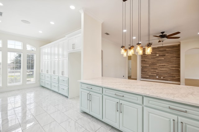 kitchen featuring ceiling fan, white cabinets, ornamental molding, decorative light fixtures, and light stone countertops