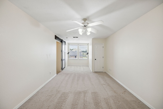 empty room featuring a barn door, ceiling fan, and light colored carpet