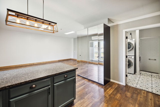 kitchen with dark stone counters, stacked washer and clothes dryer, dark hardwood / wood-style flooring, and decorative light fixtures