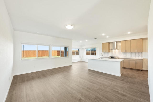 kitchen featuring tasteful backsplash, an island with sink, wall chimney exhaust hood, and dark wood-type flooring