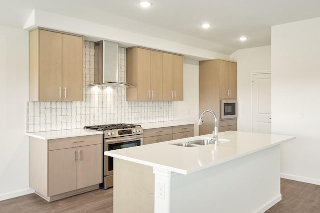 kitchen with stainless steel gas range, sink, a kitchen island with sink, and wall chimney range hood