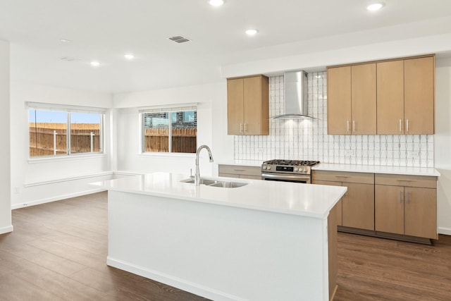 kitchen featuring wall chimney exhaust hood, high end stove, dark wood-type flooring, sink, and a center island with sink