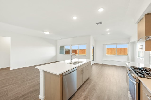 kitchen with appliances with stainless steel finishes, light brown cabinetry, sink, light hardwood / wood-style flooring, and an island with sink