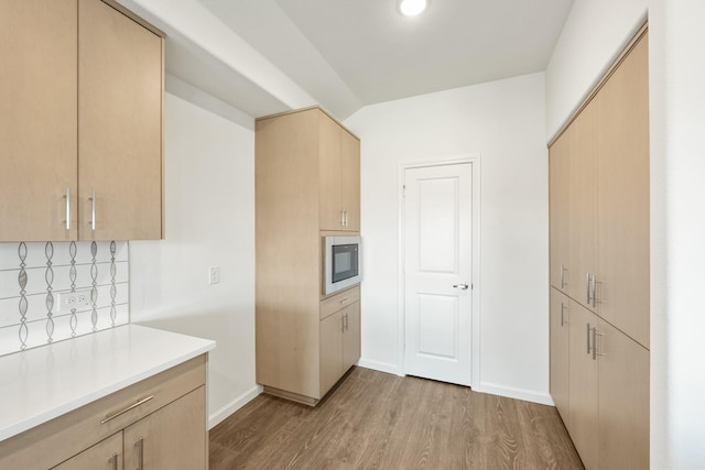 kitchen with light brown cabinets, light wood-type flooring, black microwave, and tasteful backsplash