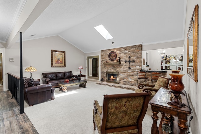 living room featuring vaulted ceiling with skylight, a brick fireplace, hardwood / wood-style flooring, a notable chandelier, and crown molding