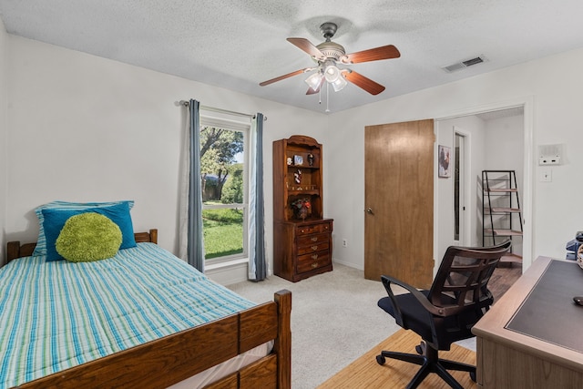 bedroom featuring ceiling fan, light colored carpet, and a textured ceiling