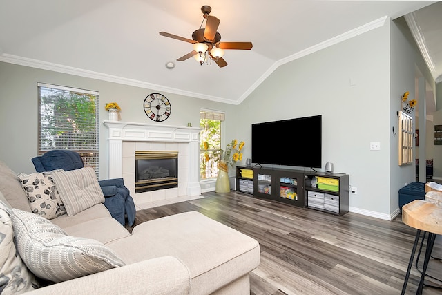 living room with ceiling fan, crown molding, a tiled fireplace, and wood-type flooring