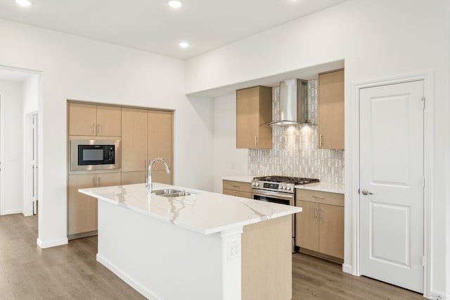 kitchen featuring sink, wall chimney exhaust hood, an island with sink, light hardwood / wood-style floors, and stainless steel range with gas stovetop