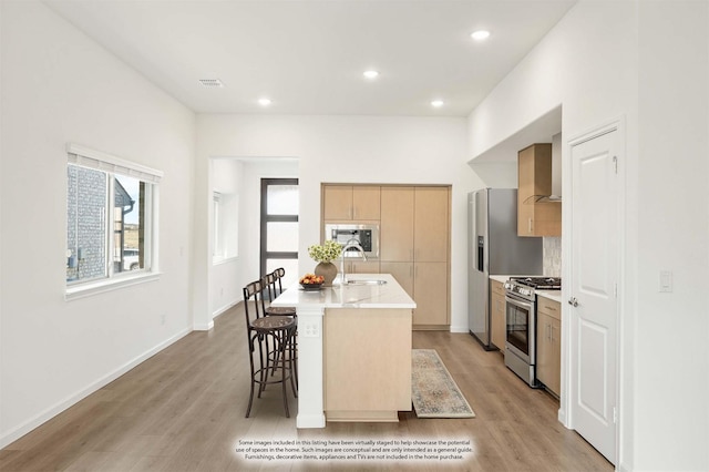 kitchen with a kitchen island with sink, sink, a breakfast bar area, light hardwood / wood-style floors, and stainless steel appliances