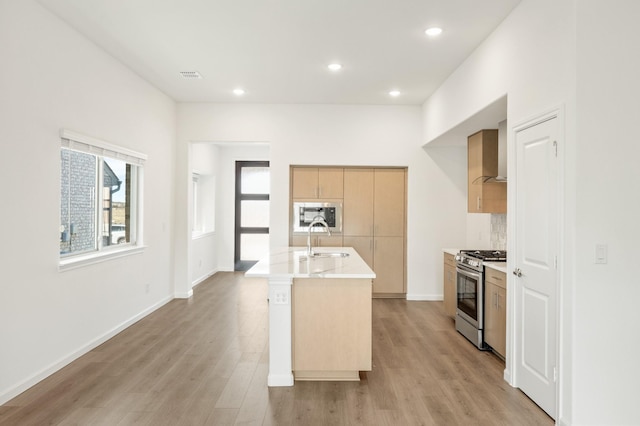 kitchen featuring stainless steel gas range, built in microwave, a kitchen island with sink, sink, and light hardwood / wood-style floors