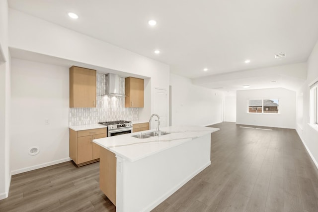 kitchen with hardwood / wood-style floors, sink, gas range, wall chimney exhaust hood, and an island with sink