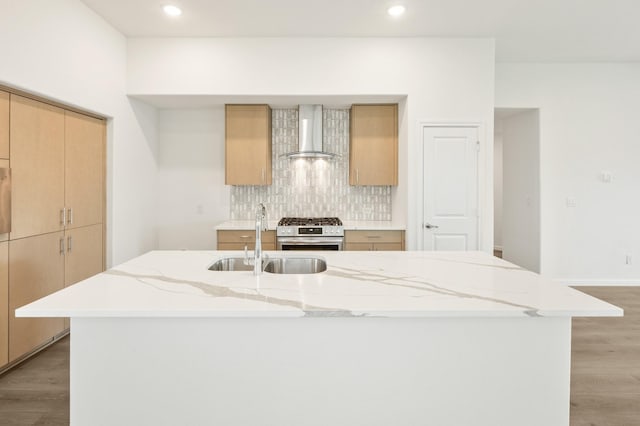 kitchen featuring wall chimney exhaust hood, sink, an island with sink, and stainless steel range with gas stovetop