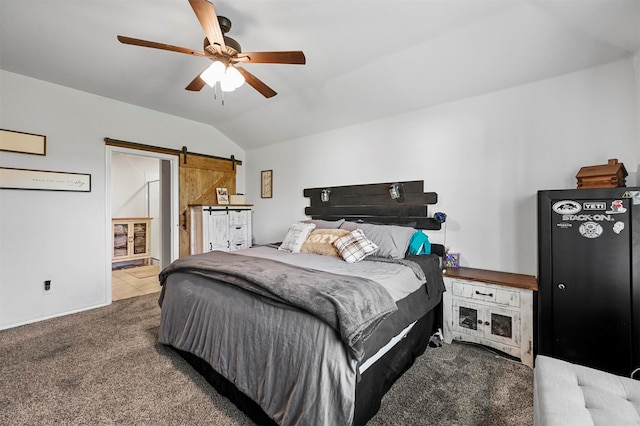 carpeted bedroom with a barn door, vaulted ceiling, ensuite bath, and ceiling fan