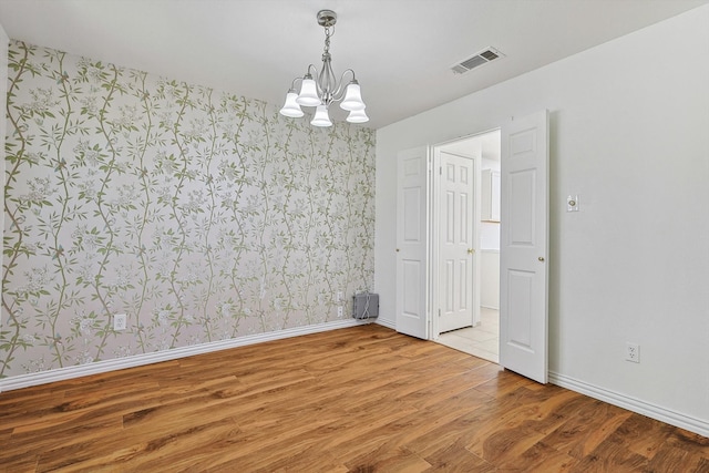 unfurnished room with an inviting chandelier and hardwood / wood-style floors