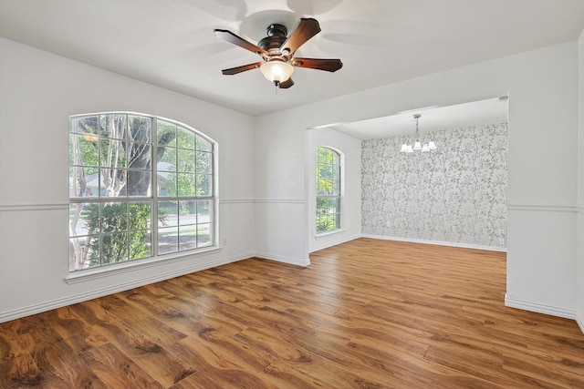 spare room featuring wood-type flooring and ceiling fan with notable chandelier