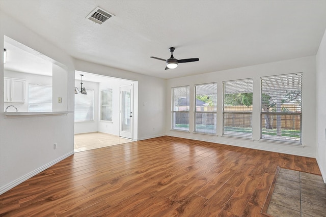 unfurnished living room featuring ceiling fan with notable chandelier and wood-type flooring