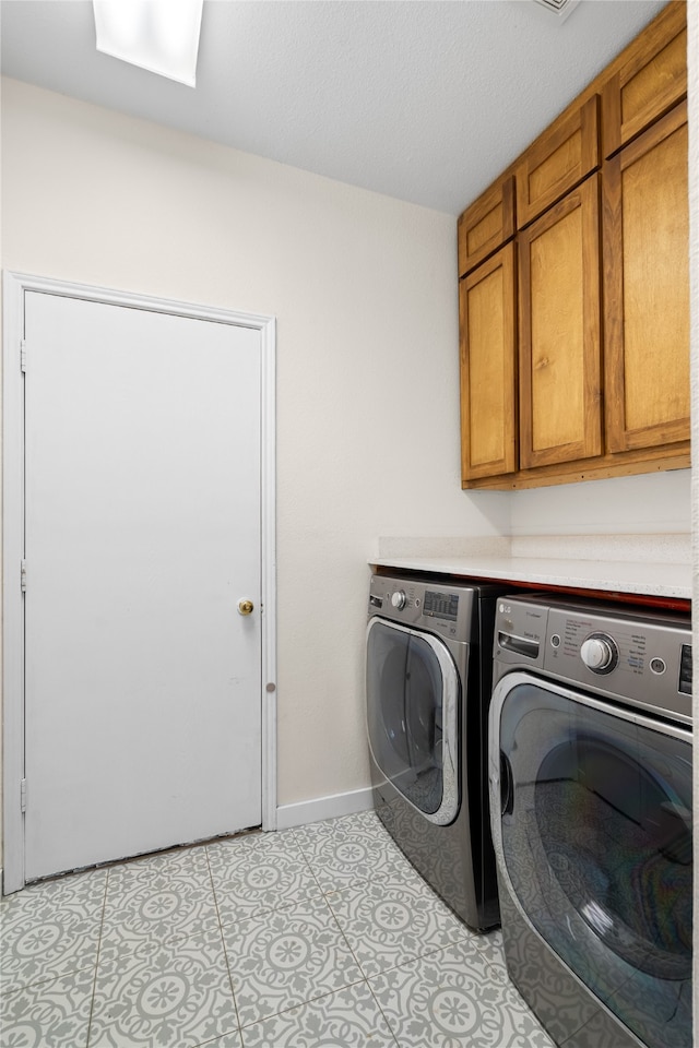 laundry area with washing machine and clothes dryer, a textured ceiling, cabinets, and light tile patterned floors