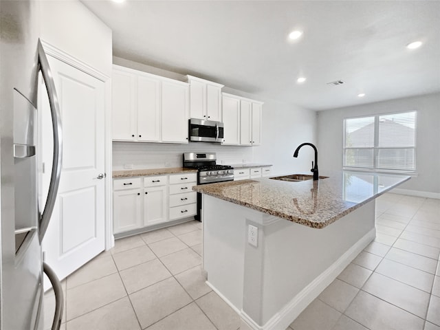 kitchen with white cabinetry, light stone countertops, stainless steel appliances, a kitchen island with sink, and sink