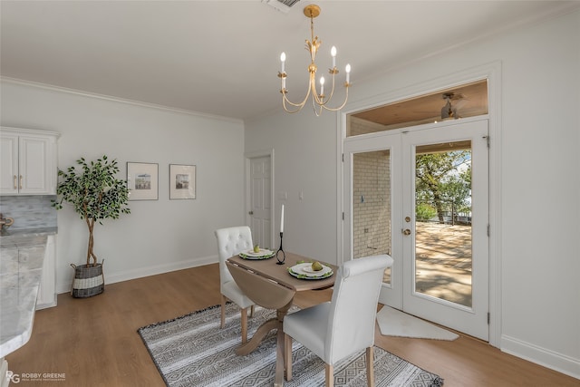 dining space with french doors, a notable chandelier, light wood-type flooring, and ornamental molding