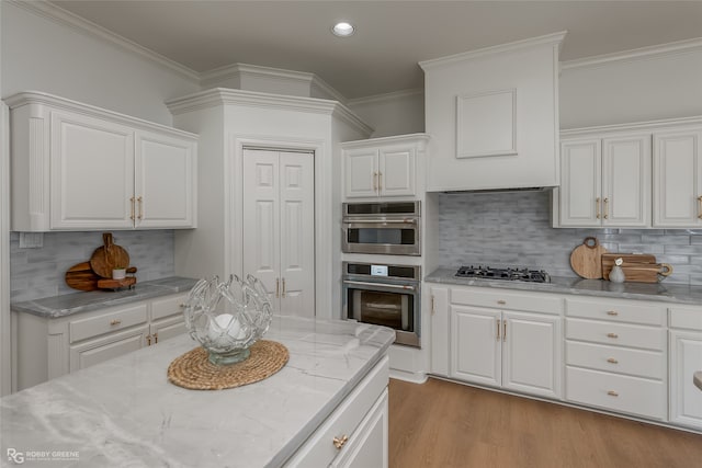 kitchen featuring white cabinets, light stone countertops, tasteful backsplash, light wood-type flooring, and crown molding