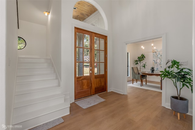 foyer entrance featuring french doors, light hardwood / wood-style flooring, a chandelier, and a high ceiling