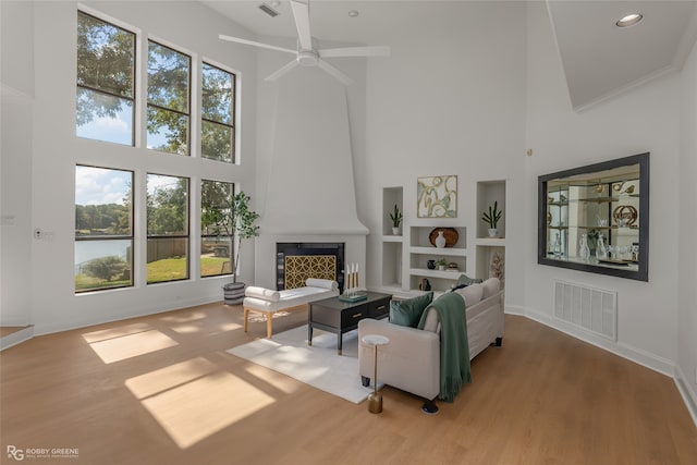 living room with a towering ceiling, light wood-type flooring, a fireplace, and ceiling fan