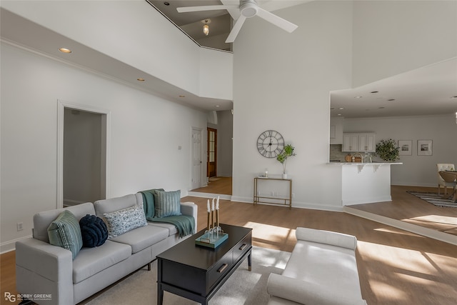 living room featuring ceiling fan, light wood-type flooring, and a towering ceiling