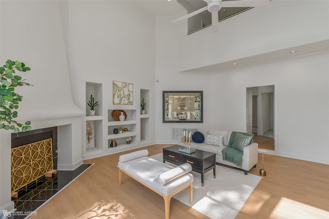 living room with ceiling fan, dark wood-type flooring, built in shelves, and a high ceiling