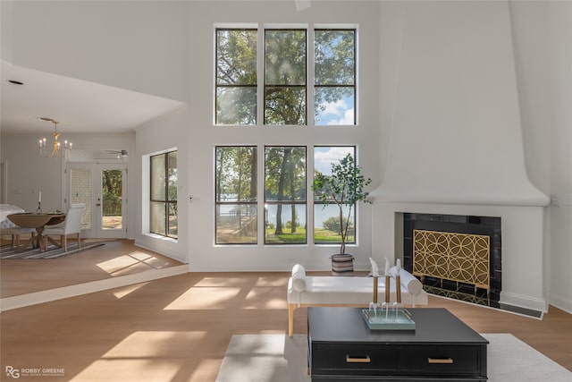 living room with a towering ceiling, a tile fireplace, a chandelier, and light hardwood / wood-style flooring