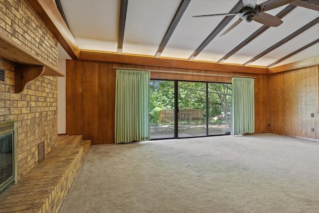 unfurnished living room featuring carpet floors, wood walls, ceiling fan, and a brick fireplace