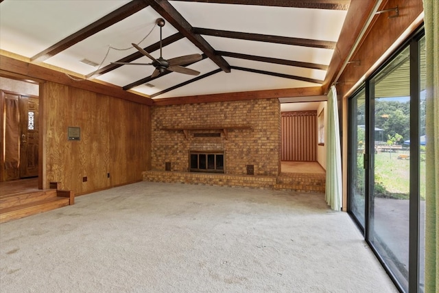 unfurnished living room with lofted ceiling with beams, wood walls, light colored carpet, a brick fireplace, and ceiling fan