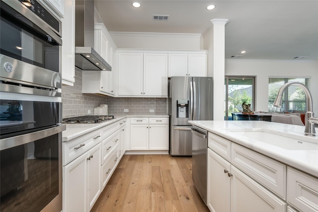 kitchen featuring appliances with stainless steel finishes, white cabinetry, wall chimney exhaust hood, and sink