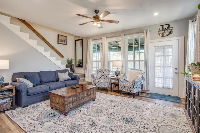 living area with light wood-type flooring, stairs, and a ceiling fan