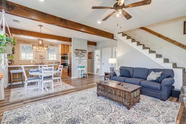 living room with beam ceiling, visible vents, stairway, and light wood finished floors