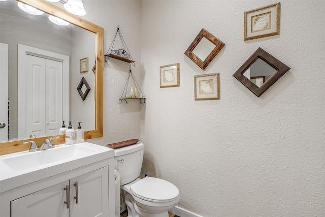 half bath featuring toilet, vanity, a closet, and a textured wall