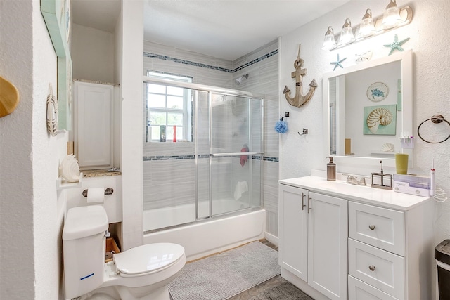 full bathroom featuring toilet, a textured wall, bath / shower combo with glass door, and vanity