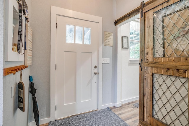 entrance foyer with baseboards, a textured wall, light wood finished floors, and a barn door