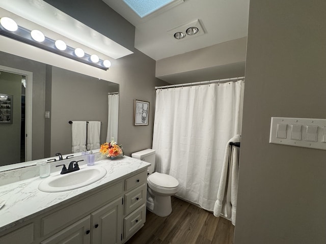 bathroom with hardwood / wood-style floors, vanity, toilet, and a skylight