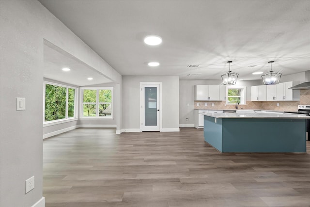 kitchen featuring stainless steel range with electric cooktop, backsplash, a kitchen island, baseboards, and white cabinets