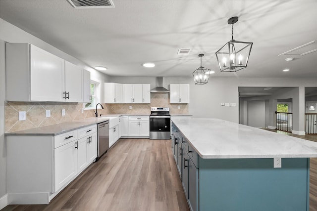 kitchen featuring wood finished floors, appliances with stainless steel finishes, a kitchen island, wall chimney range hood, and white cabinetry